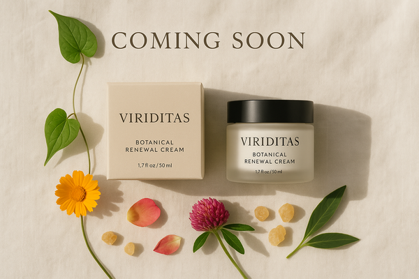 Minimalist high-end product display — Viriditas Botanical Renewal Cream jar with matching box, styled on a soft cream linen background with gentle natural daylight. A subtle overlay text in elegant serif font reads ‘COMING SOON’. Botanical elements (wild yam vine, calendula flower, red clover blossom, rose petals, frankincense resin) arranged delicately around the product. Clean composition, muted earth tones, luxury skincare aesthetic.