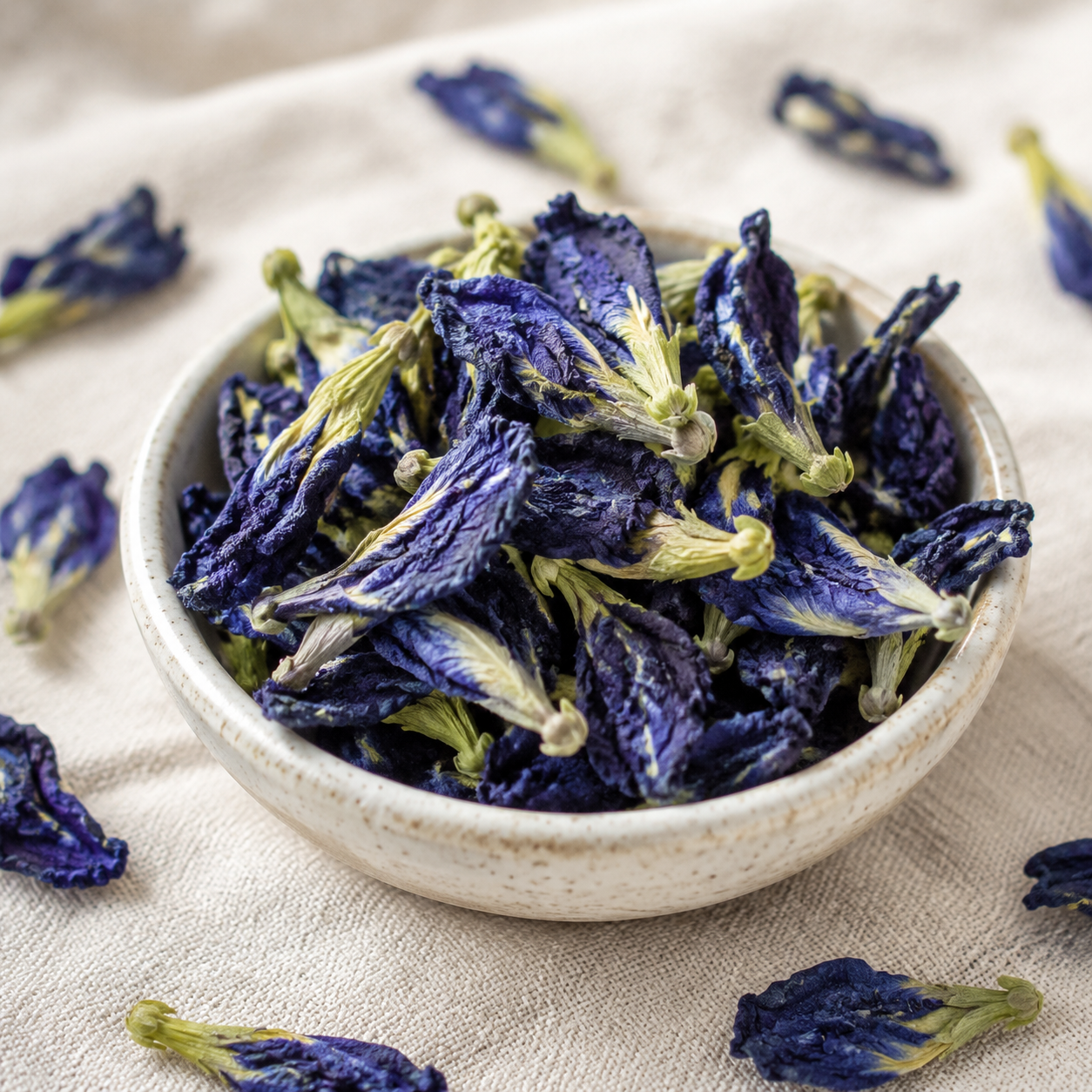 Close-up of dried Blue Butterfly Pea Flowers in a cream ceramic bowl on natural ivory linen.