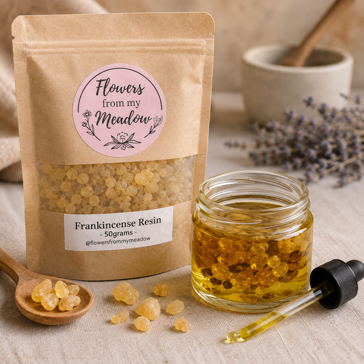 A kraft paper pouch labeled 'Flowers from my Meadow' and 'Frankincense Resin - 50grams' stands beside a small glass jar filled with amber resin pieces, with a dropper, wooden spoon, and dried lavender on a neutral fabric surface.