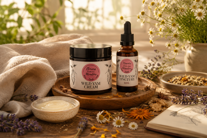 Two women wellness products from Flower from my meadow Apothecary styled on a wooden tray: a jar of Wild Yam Cream and a dropper bottle of Wild Yam Tincture, surrounded by dried flowers, herbs, a towel, and an open book in a warm, natural setting.