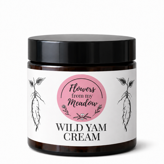 A dark amber glass jar with a black lid and a white label featuring a pink circle that reads 'Flowers from my Meadow' and 'WILD YAM CREAM' in black text, shown on a white background.