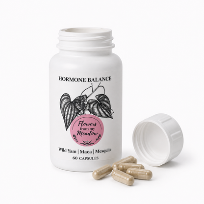A white plastic supplement bottle labeled 'HORMONE BALANCE' with 'Flowers from my Meadow' in a pink circle, shown on a white background with the cap off and several beige capsules beside it.