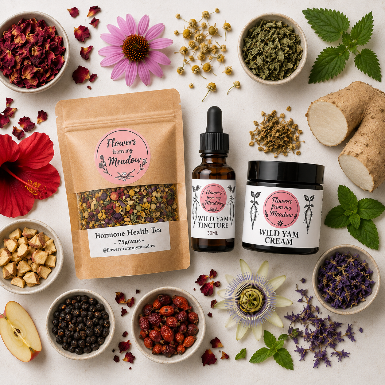 A styled flat-lay of herbal products from Flowers from my Meadow on a light beige surface, surrounded by fresh and dried botanical ingredients including green leaves, red flowers, roots, and tea components.
