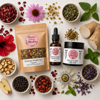 A styled flat-lay of herbal products from Flowers from my Meadow on a light beige surface, surrounded by fresh and dried botanical ingredients including green leaves, red flowers, roots, and tea components.