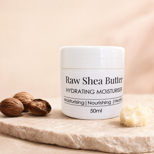 A white jar of Raw Shea Butter Hydrating Moisturiser sits on a light stone slab with whole nuts and a dollop of pale shea butter nearby, against a soft beige background.