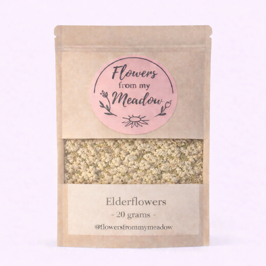 Kraft paper packaging with a pink label for 'Flowers from my Meadow' elderflowers on a light purple background.